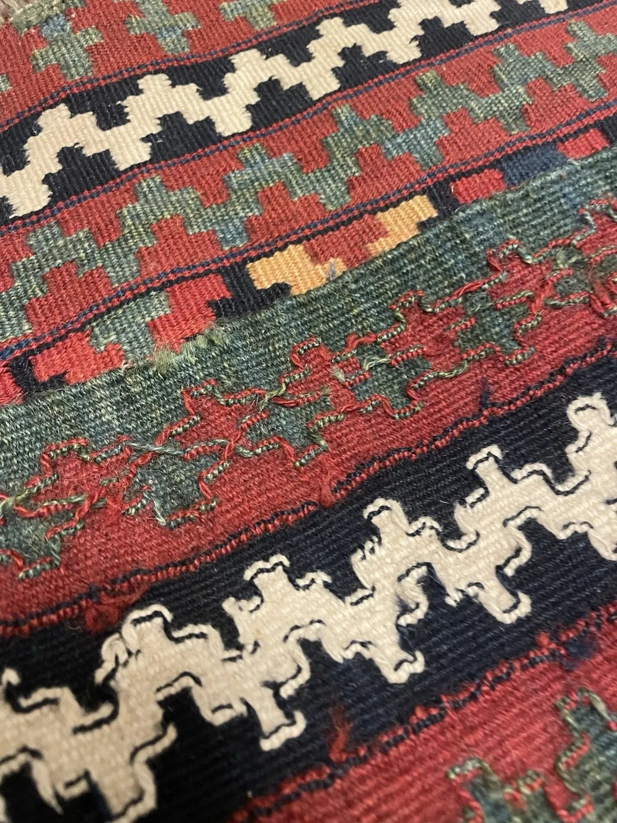Detail of the border on a Qashqai bagface kilim, showing an ivory stepped hook guard border (kochanak) on black, a deep crimson main border with geometric accents, and an olive green outer sawtooth frame.

