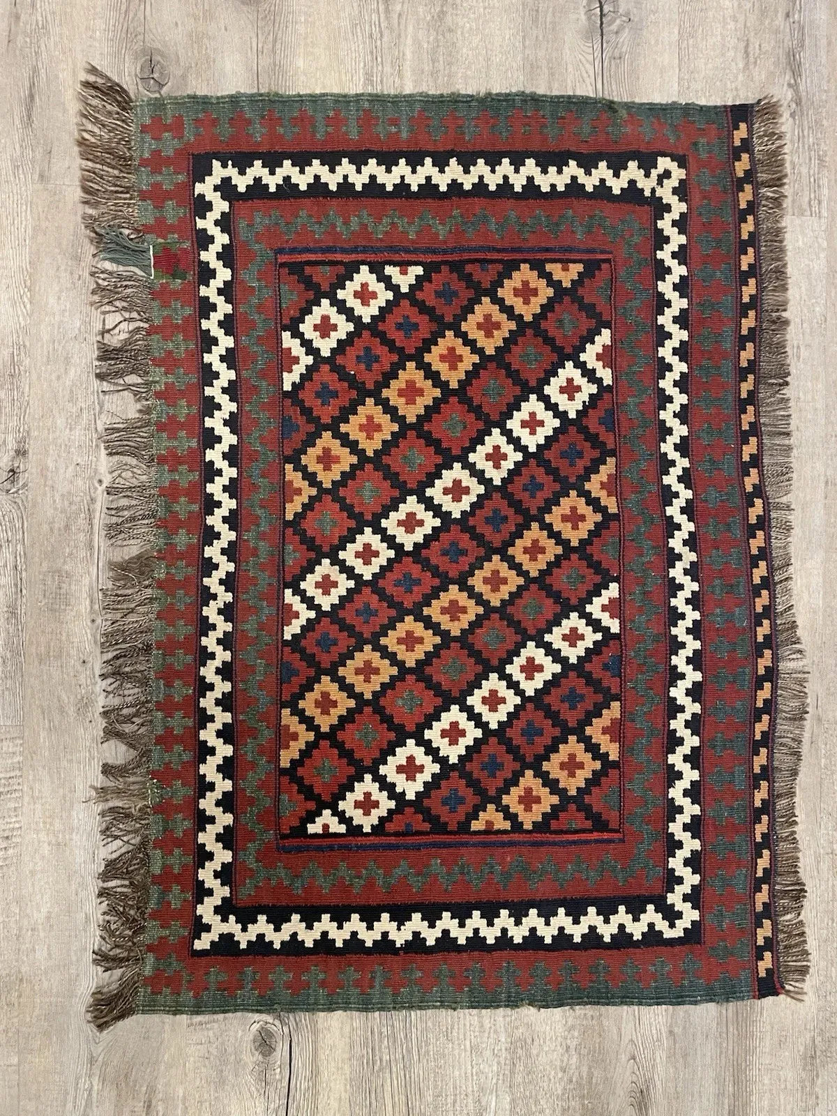 Full view of an antique Qashqai tribal flatweave with an all-over diamond lattice design in jewel tones of red, gold, white, and blue against a jet black ground, ideal for framing and wall display.

