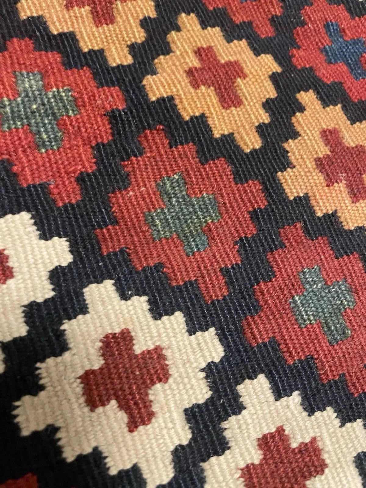 Close-up of the diamond lattice motif on an antique Qashqai kilim, showing the rotating palette of madder crimson, amber gold, ivory, and indigo creating a shimmering, jewel-like surface.

