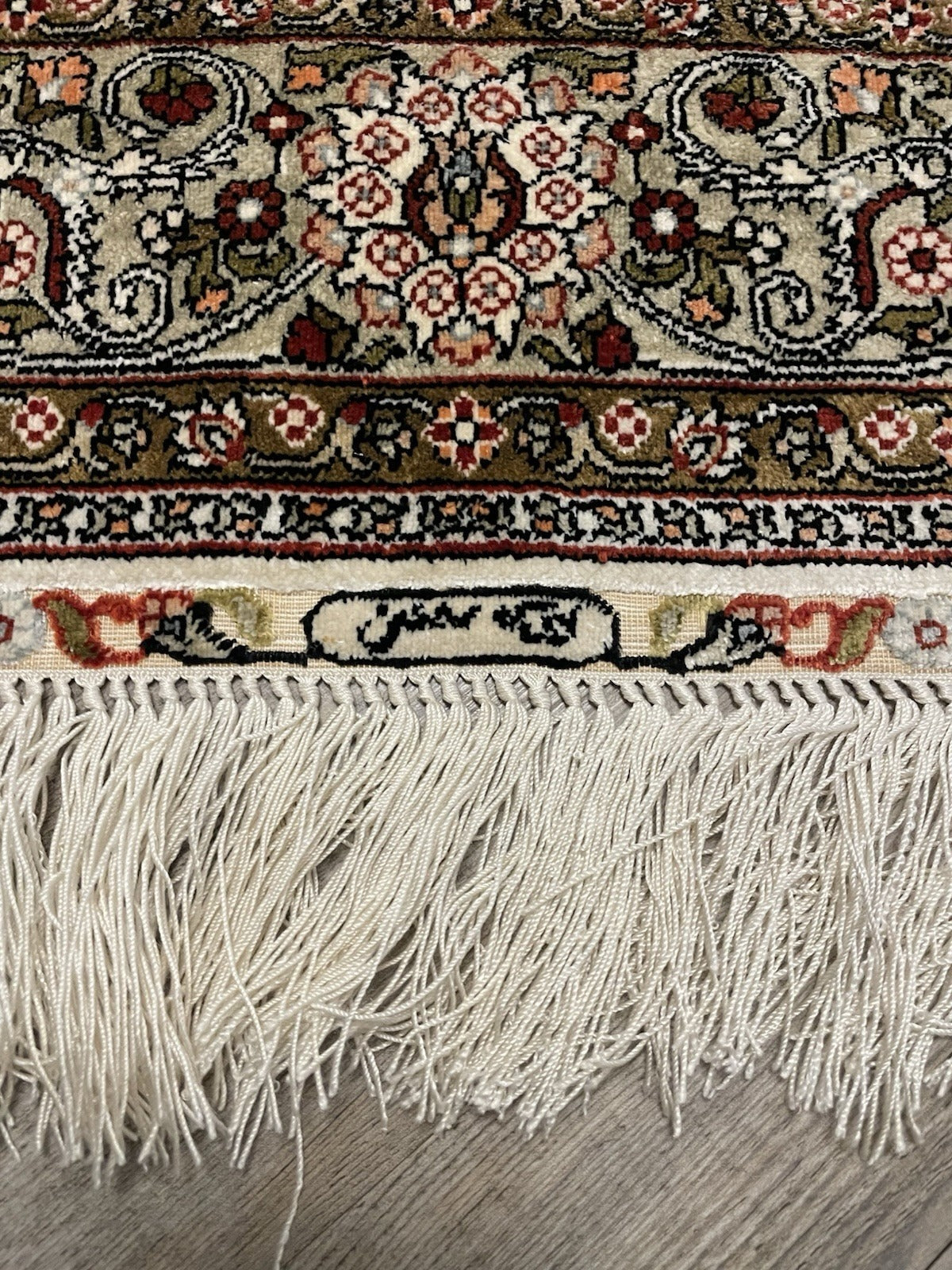 Detail of the olive-green main border on a Turkish Hereke silk rug, showing a continuous arabesque scroll of ivory stems and palmettes with inner and outer ivory guard borders of running floral vines.

