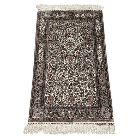 Full view of a vintage Turkish Hereke silk prayer rug from the 1970s, featuring a pointed mihrab arch on an ivory ground with Arabic calligraphy "Allahu Akbar", a paradise bird (simurgh/phoenix) above a double-gourd vase, and an olive-green arabesque border.

