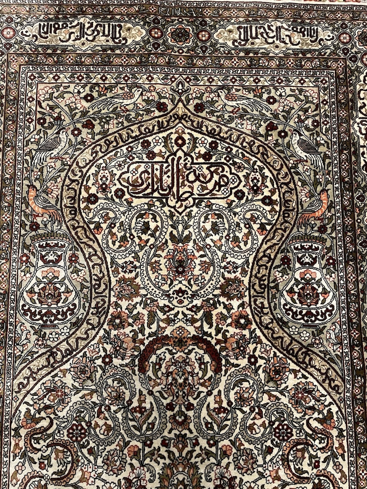 Full perspective of a collectible Hereke prayer rug displayed on a wall, demonstrating its ideal scale (124 × 77 cm) for mounting as a textile work of art with directional silk sheen.

