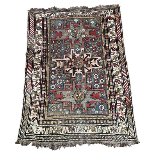 Full view of an antique Caucasian Shirvan rug from circa 1900, featuring a large stepped cross medallion in ivory on a deep steel blue indigo ground, surrounded by all-over scatter of small crimson and ivory floral rosettes.

