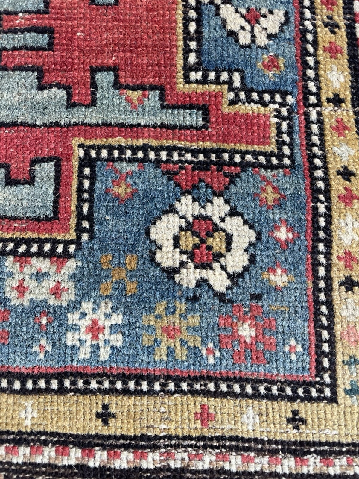 Antique Caucasian geometric rug with a large stepped cross/star medallion in ivory, outlined with a fine pearl-bead border and a small rosette cartouche at the center, on a steel blue field.

