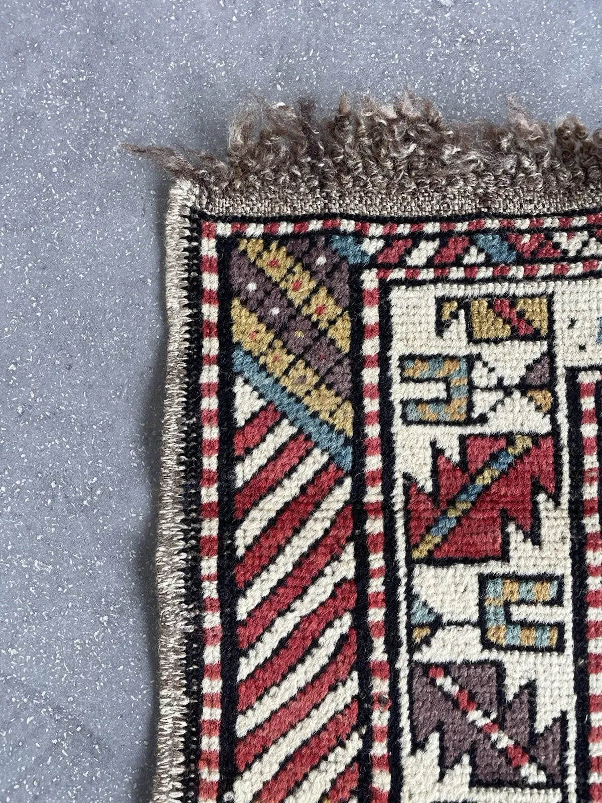 Close-up of an antique Shirvan rug showing the central stepped cross medallion with four projecting arms, each terminating in a characteristic Caucasian stepped hook, outlined in black with a pearl-bead inner border.

