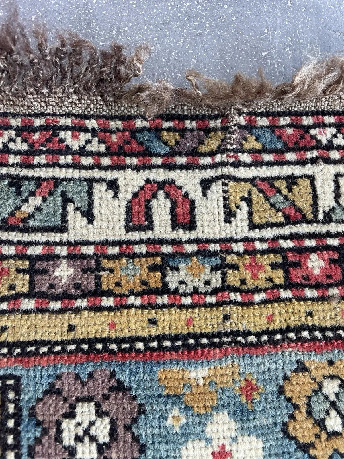 Detail of the main border on a Shirvan rug from the eastern Caucasus, featuring a bold stepped geometric meander in crimson and ivory on a warm camel gold ground, with black inner and outer guard borders.

