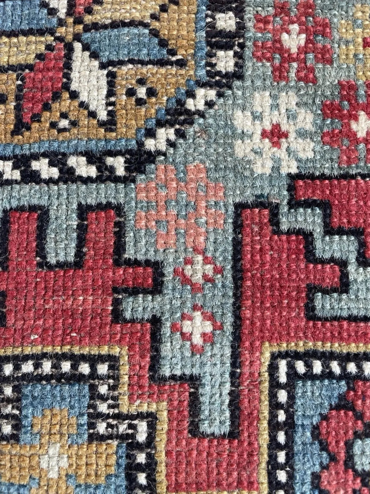 Full view of a circa 1900 Shirvan tribal rug with large stepped corner forms in madder crimson with pale grey-blue infill, and small animal or bird silhouettes punctuating the field corners.

