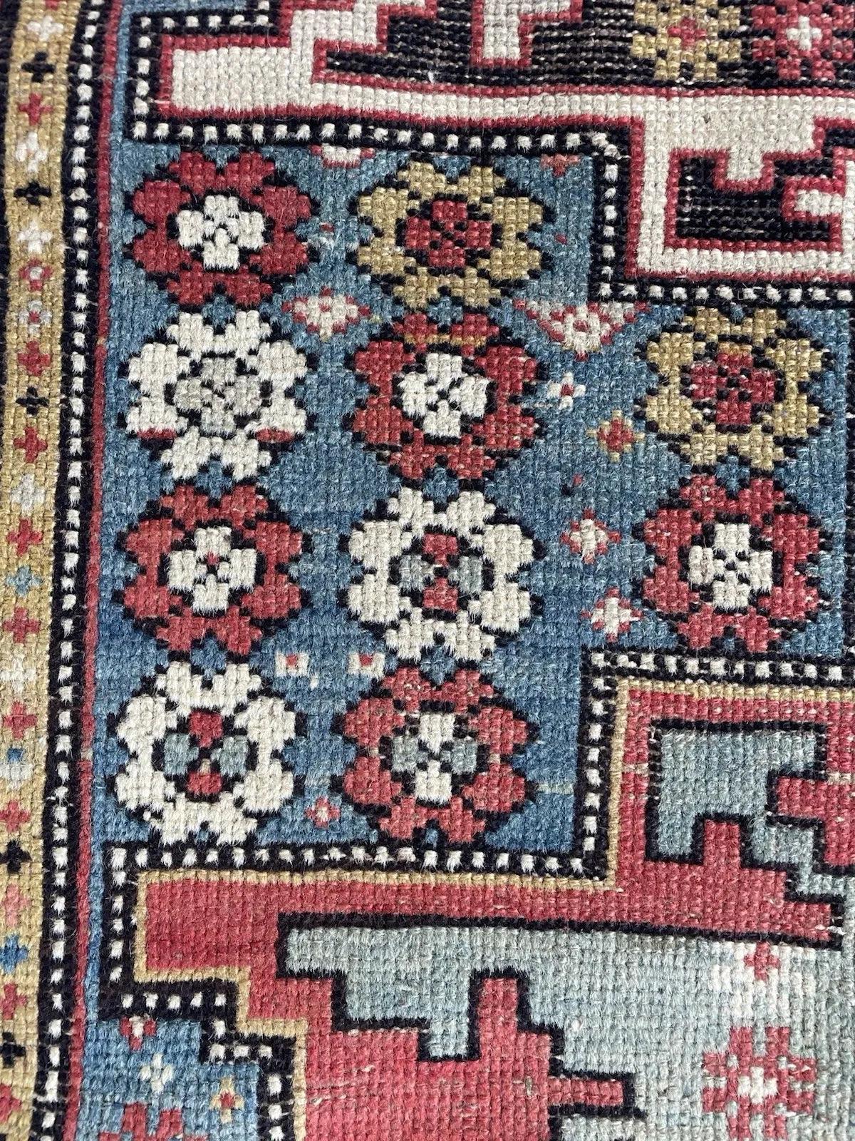 Close-up of the all-over rosette scatter field on an antique Shirvan carpet, showing alternating crimson and ivory floral motifs with gold and olive accents arranged across the natural indigo blue ground.

