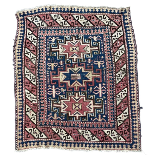 Full view of an antique Caucasian Kazak rug from circa 1880, featuring a large stepped polygon medallion in dusty rose antique pink on a deep royal blue indigo ground, with an ivory stepped cross and blue amulet gul at the center.

