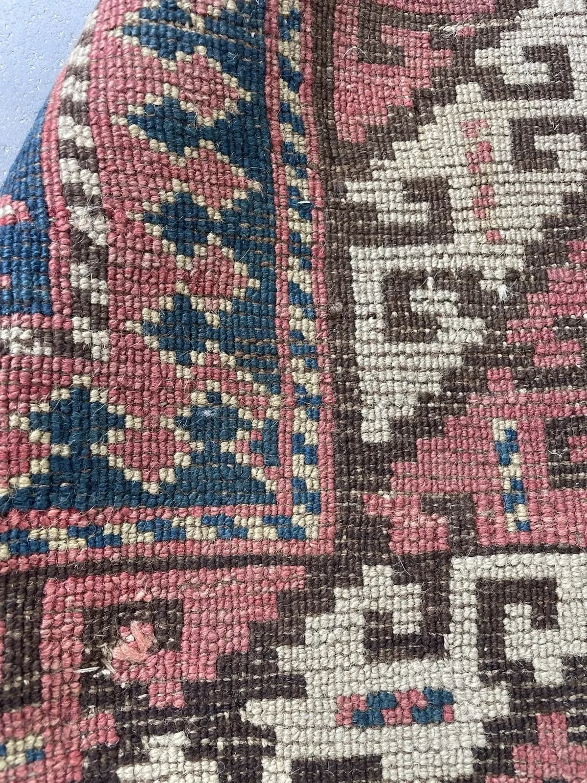 Detail of the dusty rose main border on a Kazak rug, showing a bold stepped geometric vine in dark brown and ivory on a pink ground, framed by dark brown inner and outer guard borders with ivory reciprocal hook meanders.

