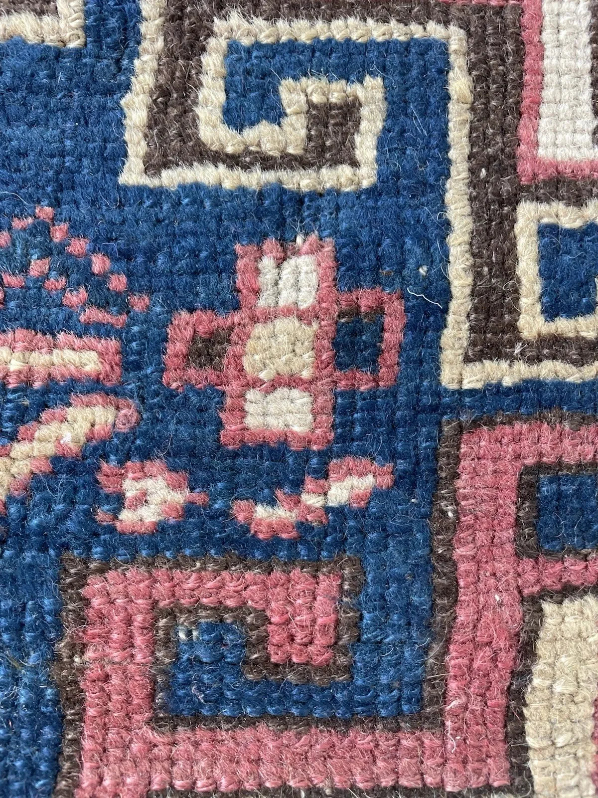 Close-up of the characteristic "Kazak pink" medallion – the specific dusty rose of oxidized madder on high-altitude Caucasian wool – outlined in dark brown with a crisp ivory pearl-bead border.

