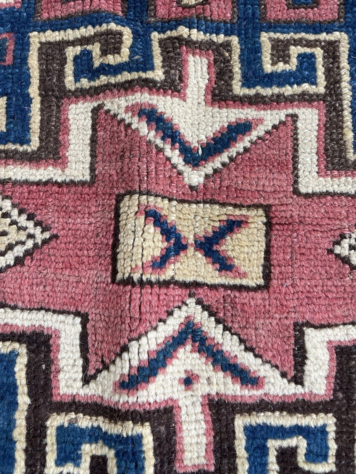 Close-up of the field scatter on an 1880s Kazak carpet, showing small geometric filler motifs and stylized animal/bird silhouettes rendered with the bold, slightly naive energy of authentic tribal weaving.


