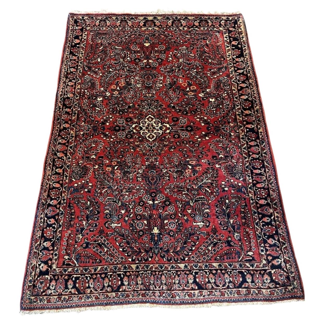 Full view of an antique handmade Sarouk wool rug from the 1920s featuring a crimson red field, central eight-pointed star medallion, and allover floral spray design.

