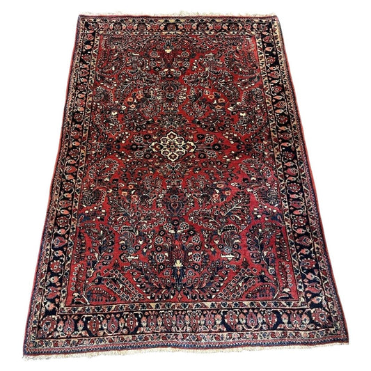 Full view of an antique handmade Sarouk wool rug from the 1920s featuring a crimson red field, central eight-pointed star medallion, and allover floral spray design.

