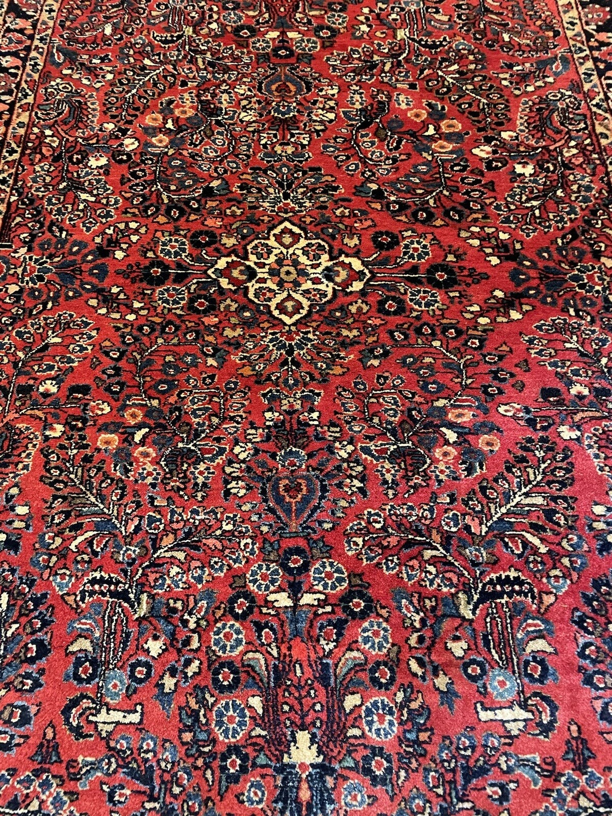 Handmade 1920s Sarouk wool rug on a cotton foundation, featuring an eight-pointed star medallion radiating into a crimson field of botanical detail.

