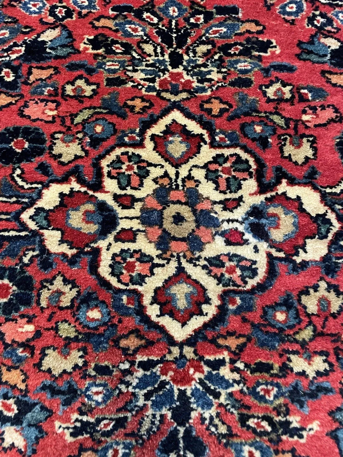 Close-up of a vintage Middle Eastern Sarouk rug showing dense curvilinear floral sprays, palmette blossoms, and vine scrolls in navy, ivory, and sage green.

