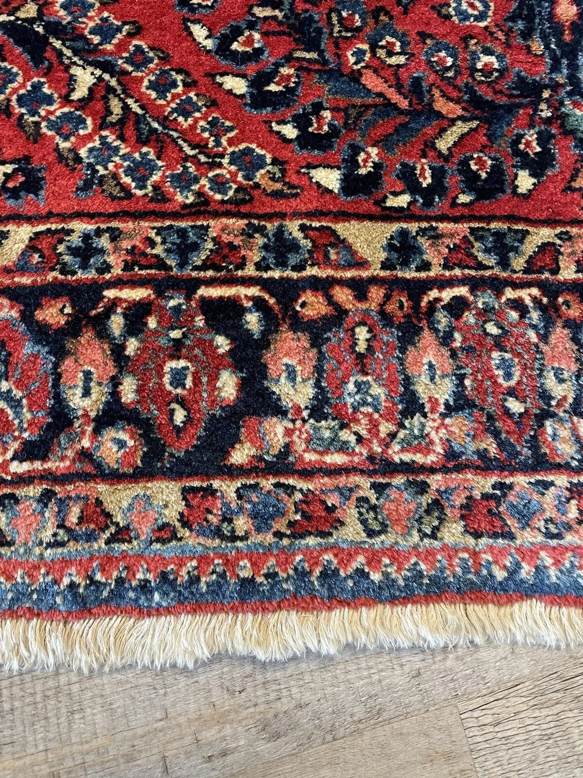 Century-old Sarouk wool rug with vivid colors including midnight navy, soft rose, sage green, and ivory on a rich crimson red ground.

