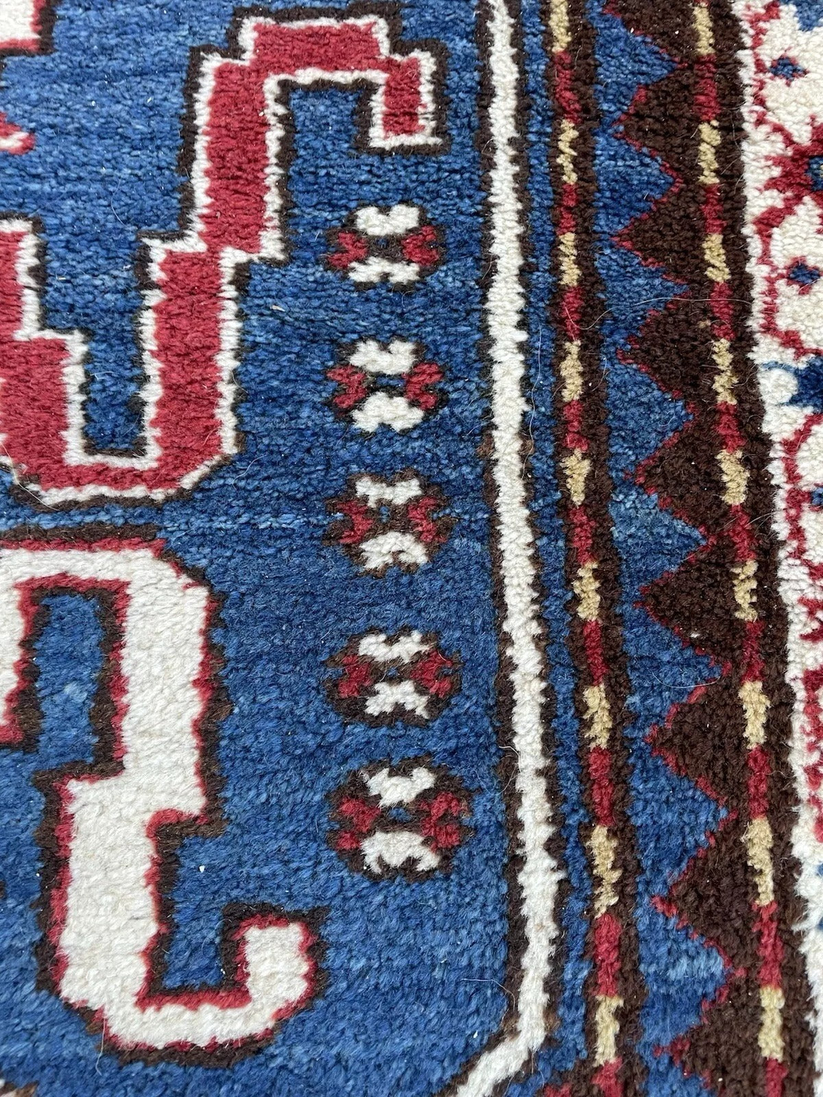 Texture close-up showing the rugged, hand-spun wool pile of the Kazak carpet.

