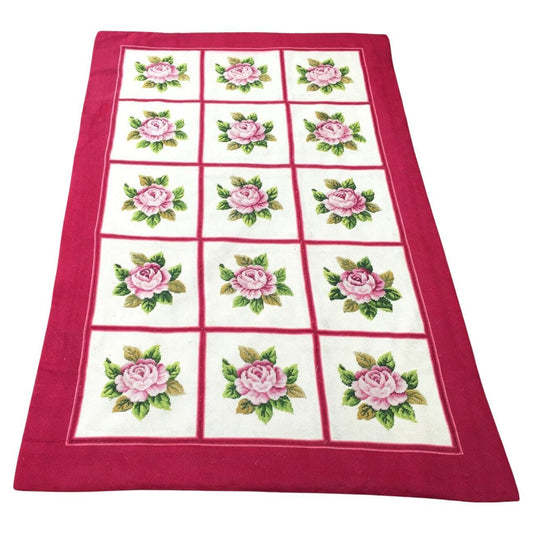 Handmade Vintage French Needlepoint Rug featuring intricately stitched pink roses with green leaves on a white grid background, bordered by bright red borders