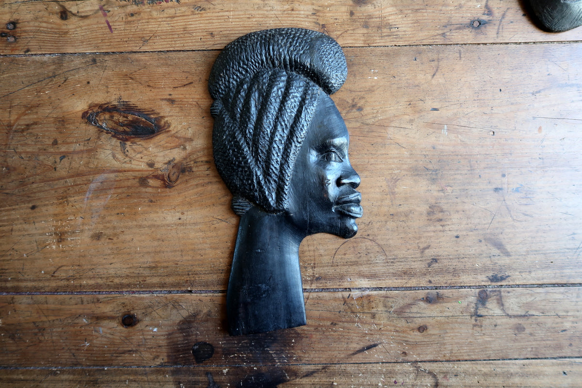 Fine carving details on the smooth brow, delicate nose line, and refined lips of an ebonized tropical hardwood profile portrait.