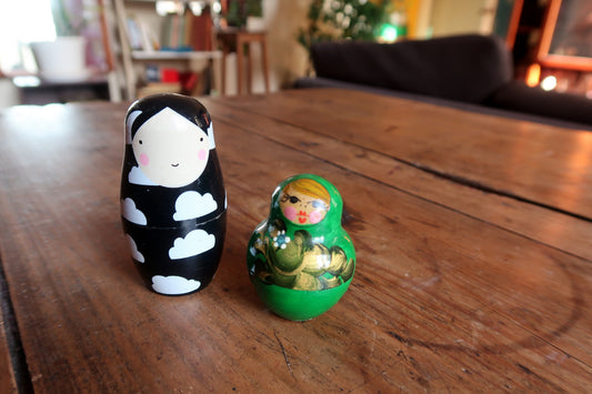 Set of two collectible wooden Matryoshka nesting doll sets displaying contrasting traditional green folk patterns and minimalist black artwork.