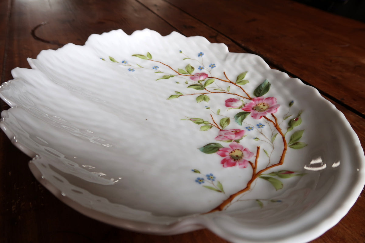 Angled close-up of pink blossoms, green leaves and blue flowers on the ribbed porcelain
