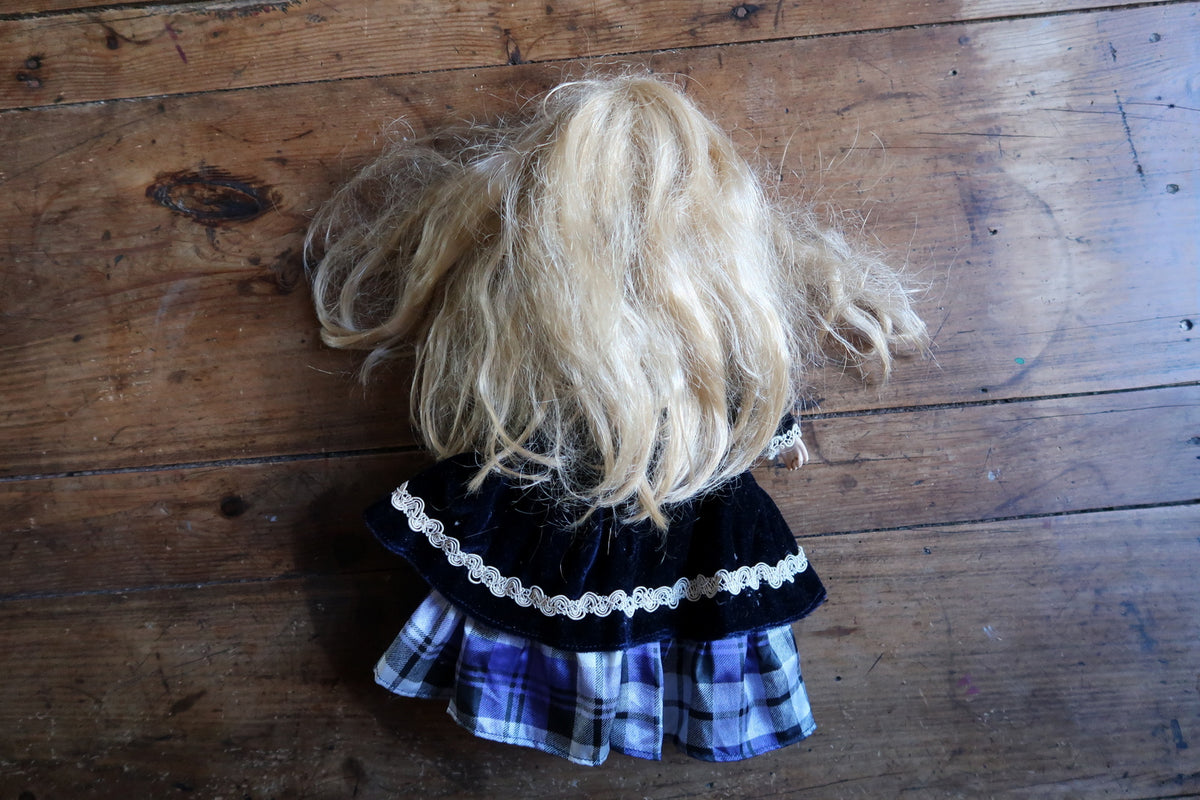 Back view of the doll with loose blonde hair and braid-trimmed navy overskirt.