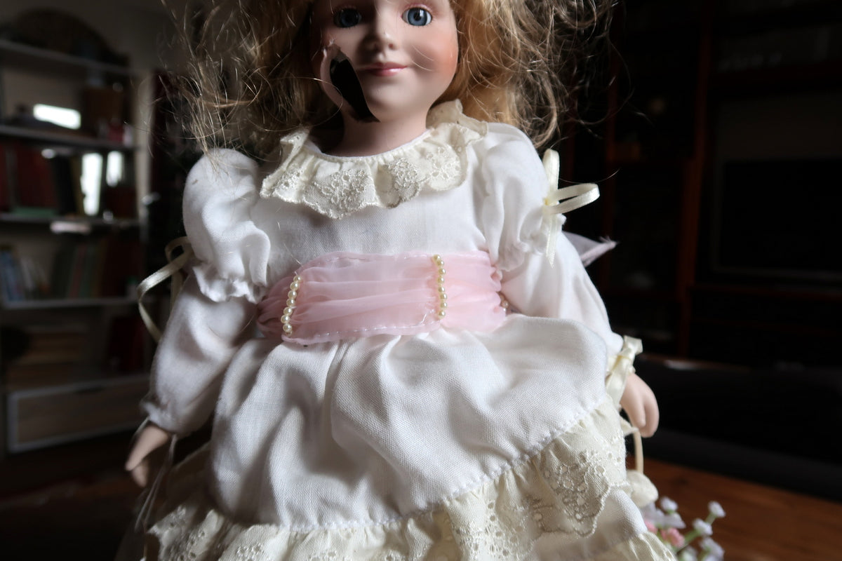 Angled view of the white dress, embroidered collar, pink sash and tangled golden-brown hair.