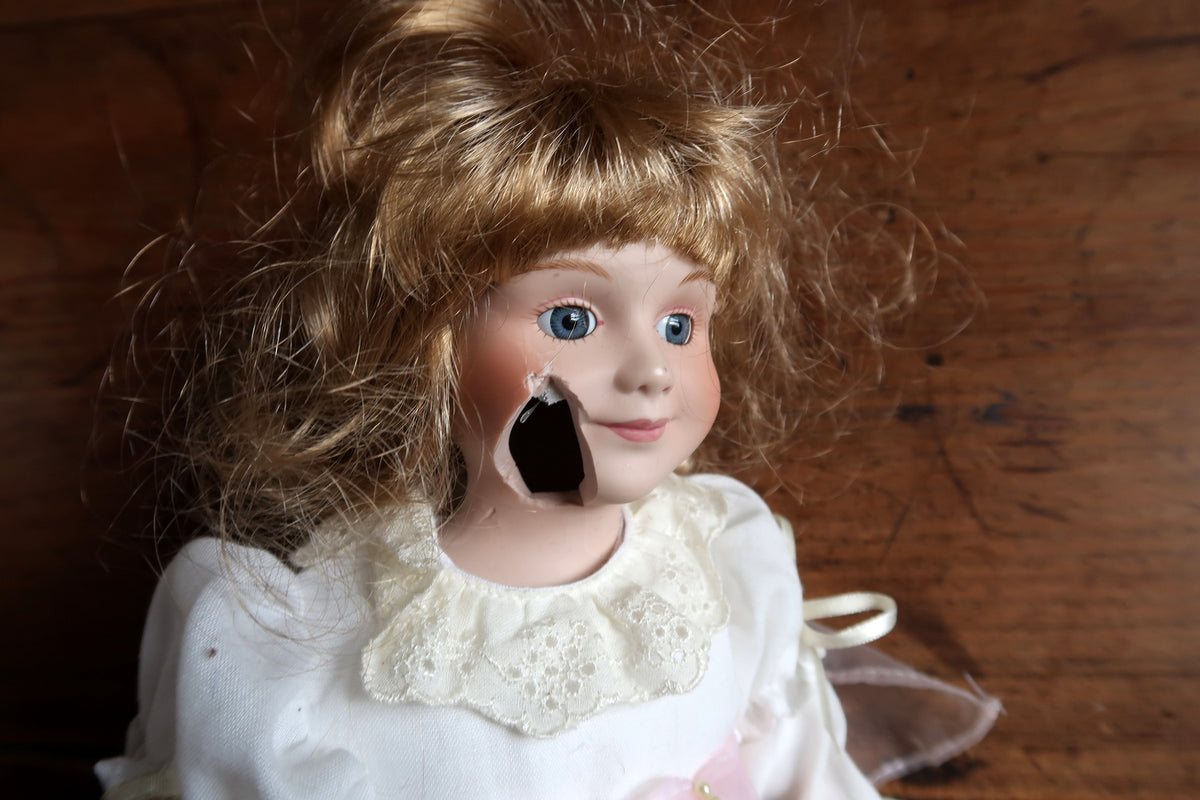 Attached round tag reading Elite Collection Porzellan beside the doll’s hand.