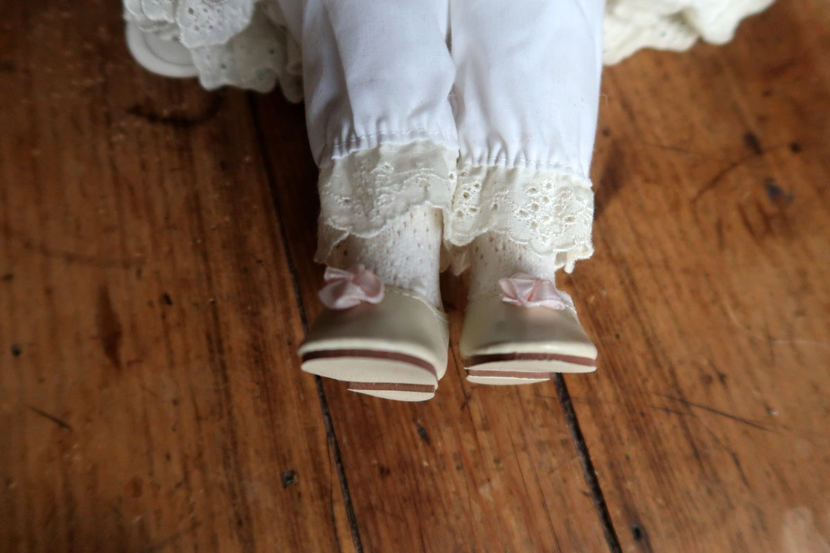 Back view of the doll showing pink sash bow, embroidered skirt and curly hair.