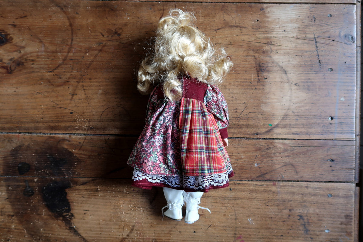 Full front view of the porcelain doll with patterned dress and ribbon-laced boots.