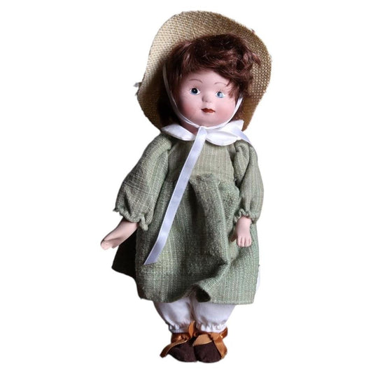 Vintage porcelain doll wearing a sage green dress, flower-trimmed woven hat and brown shoes.