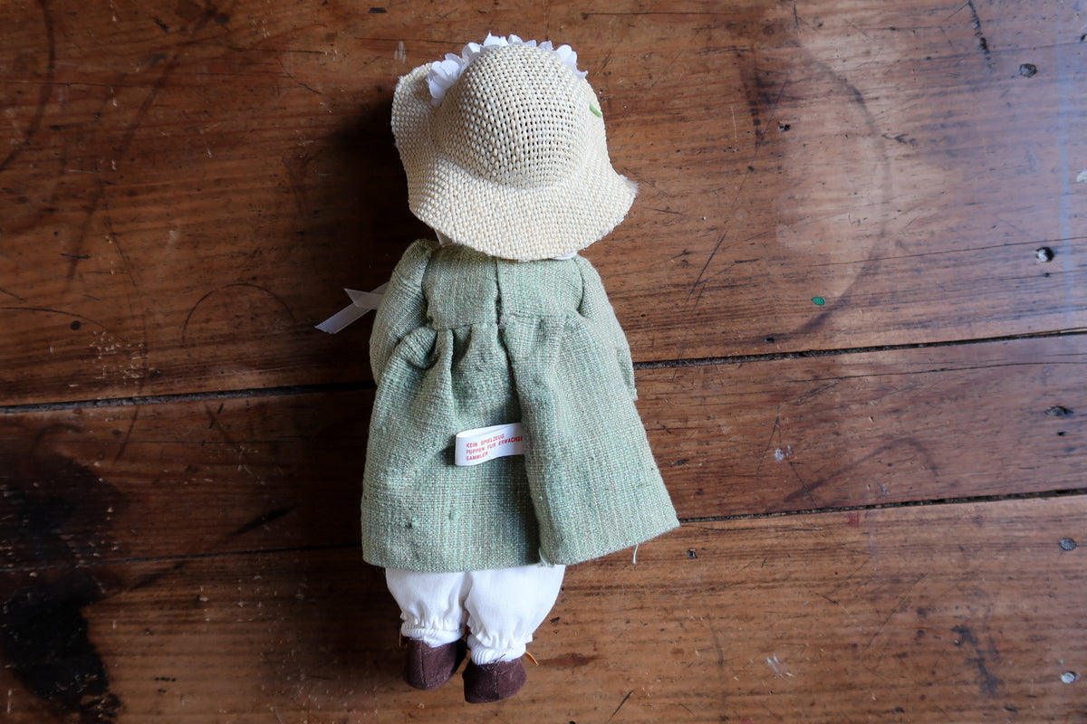 Rear view showing the woven hat, gathered green dress and attached collector label.