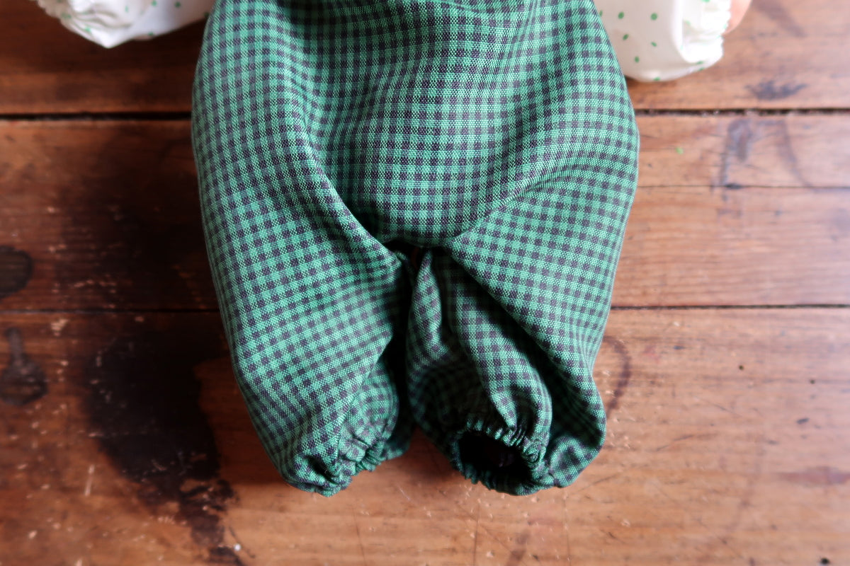 Dark leather-look brace and white button beside a gathered green-dotted sleeve.