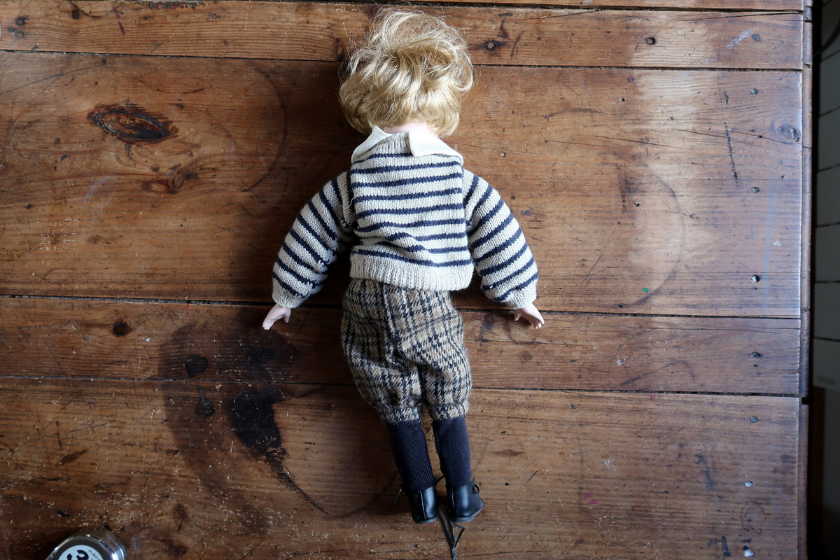 Blonde-haired doll face with painted rosy cheeks and fixed blue-grey eyes.