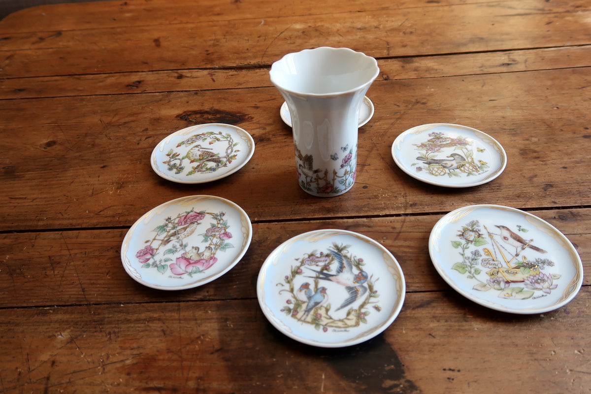 Six bird and botanical collector plates arranged around a white flared Ole Winther vase.