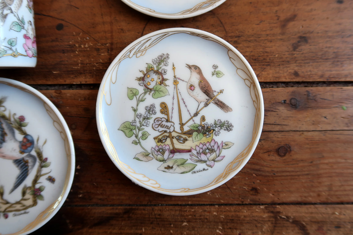 April collector plate with a songbird, lilac flowers, water lilies and gold ornamental details.