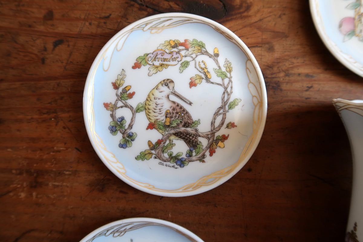 November porcelain plate showing a long-billed bird among oak leaves, acorns and blue berries.