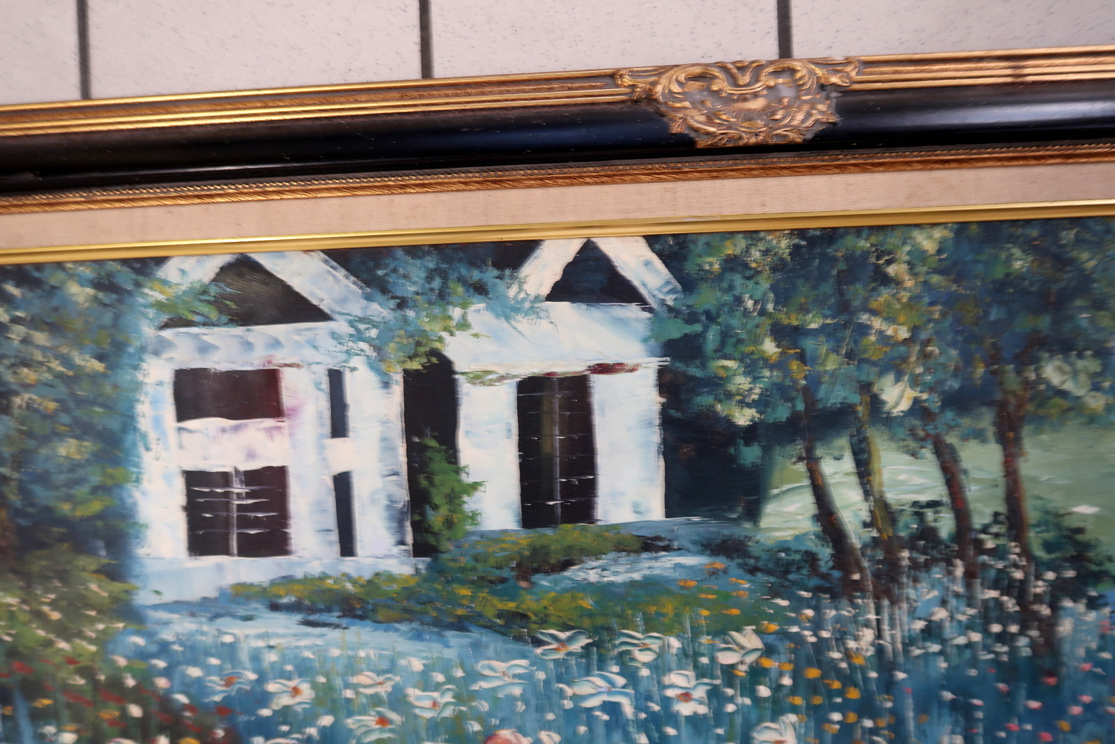 Full view of a vintage oil painting displayed in its original ornate gilded wooden frame, showing a mother and child in a peaceful rural landscape with a house, trees, and serene water.

