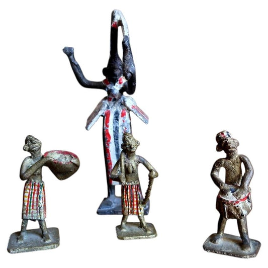 Full view of a set of 4 hand-painted French colonial lead figurines from the 1950s, including one tall ceremonial figure in a white, red, and black striped robe with arms raised overhead, and three smaller attendant figures (drummer, staff bearer, and standing figure) on square bases.

