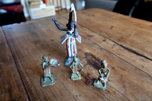 Close-up of the tall central ceremonial figure from a vintage French lead figurine set, showing dramatic white, red, and black striped ceremonial robes, black painted skin with white highlights, and arms raised holding a crescent or tusk form.

