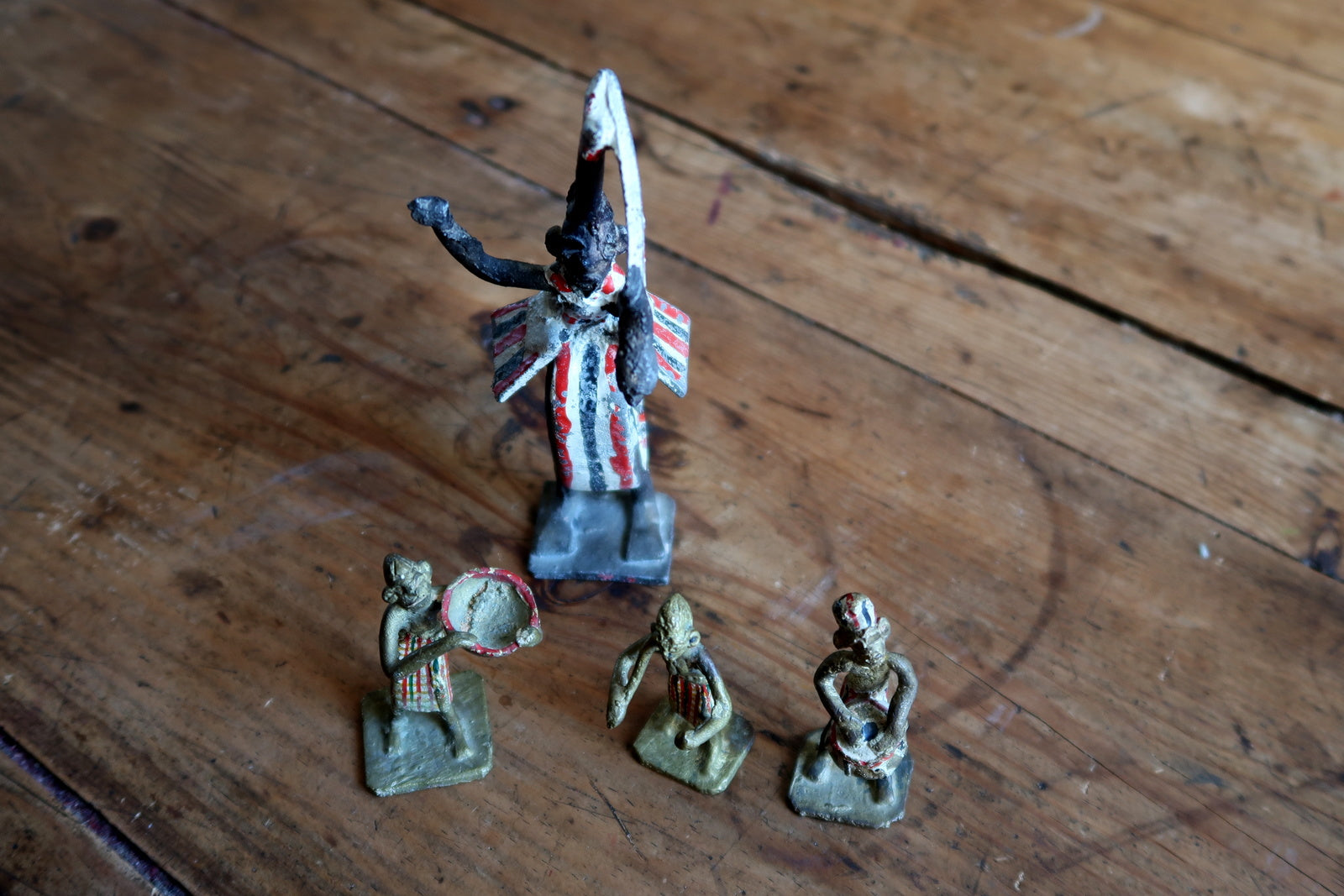 Full perspective of four hand-painted colonial-era French figurines displayed as a group, showing the central 15cm ceremonial figure with arms raised and three 6cm attendants with staff, drum, and standing pose, all on square bases.

