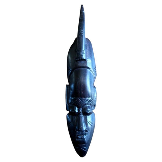 Front view of a finely carved miniature West African face mask in ebonized hardwood, mid-20th century, featuring an elongated narrow face with a tall sharply pointed horn or crest rising from the crown, almond-shaped eyes, and geometric scarification marks on forehead and chin – measuring 20 cm in height.

