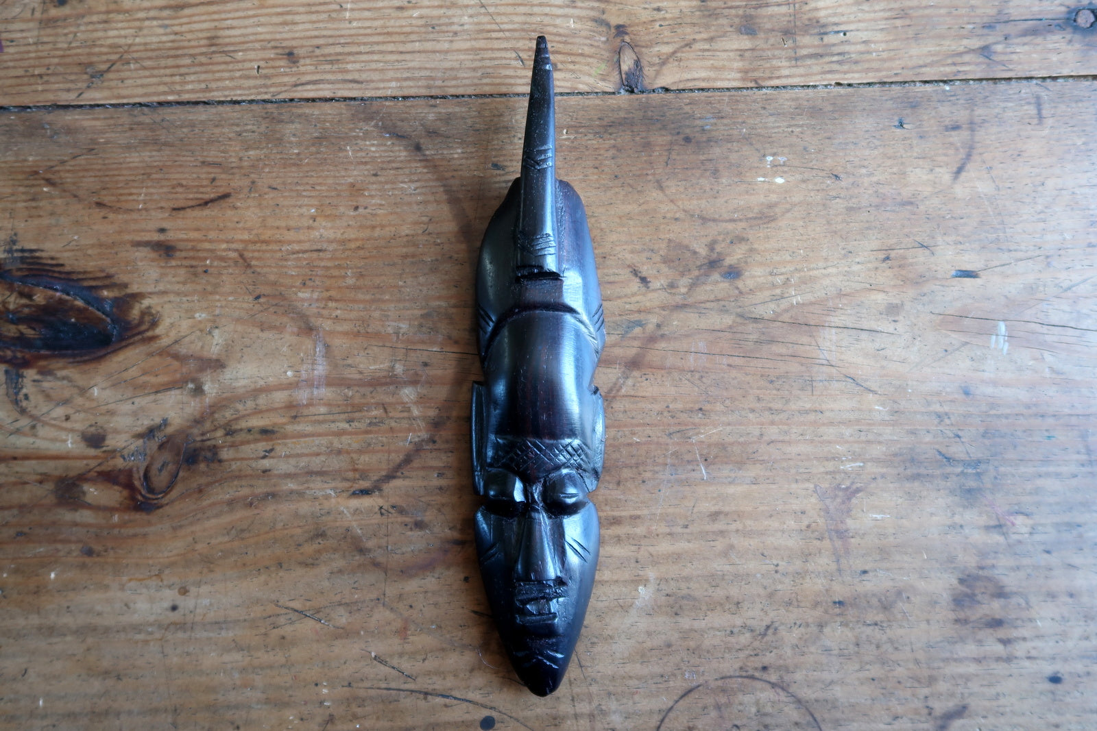 Full view of a small African ceremonial-style mask adapted for the decorative export market, mid-20th century, ebonized hardwood with pointed crest, closed eyes, and refined carving – ideal for gallery wall grouping or collector's cabinet.

