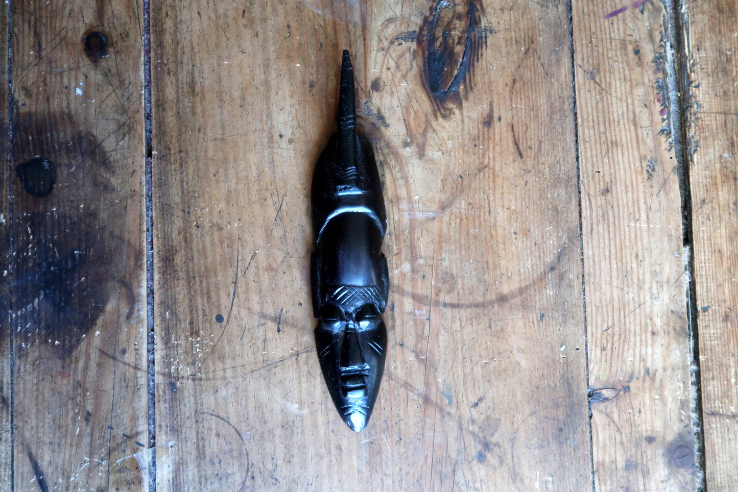 Close-up of a carved ebonized wood mask from Côte d'Ivoire or Ghana, showing the Baoulé-influenced aesthetic with long straight nose, closed almond eyes, small composed mouth, and polished black surface with warm undertones.


