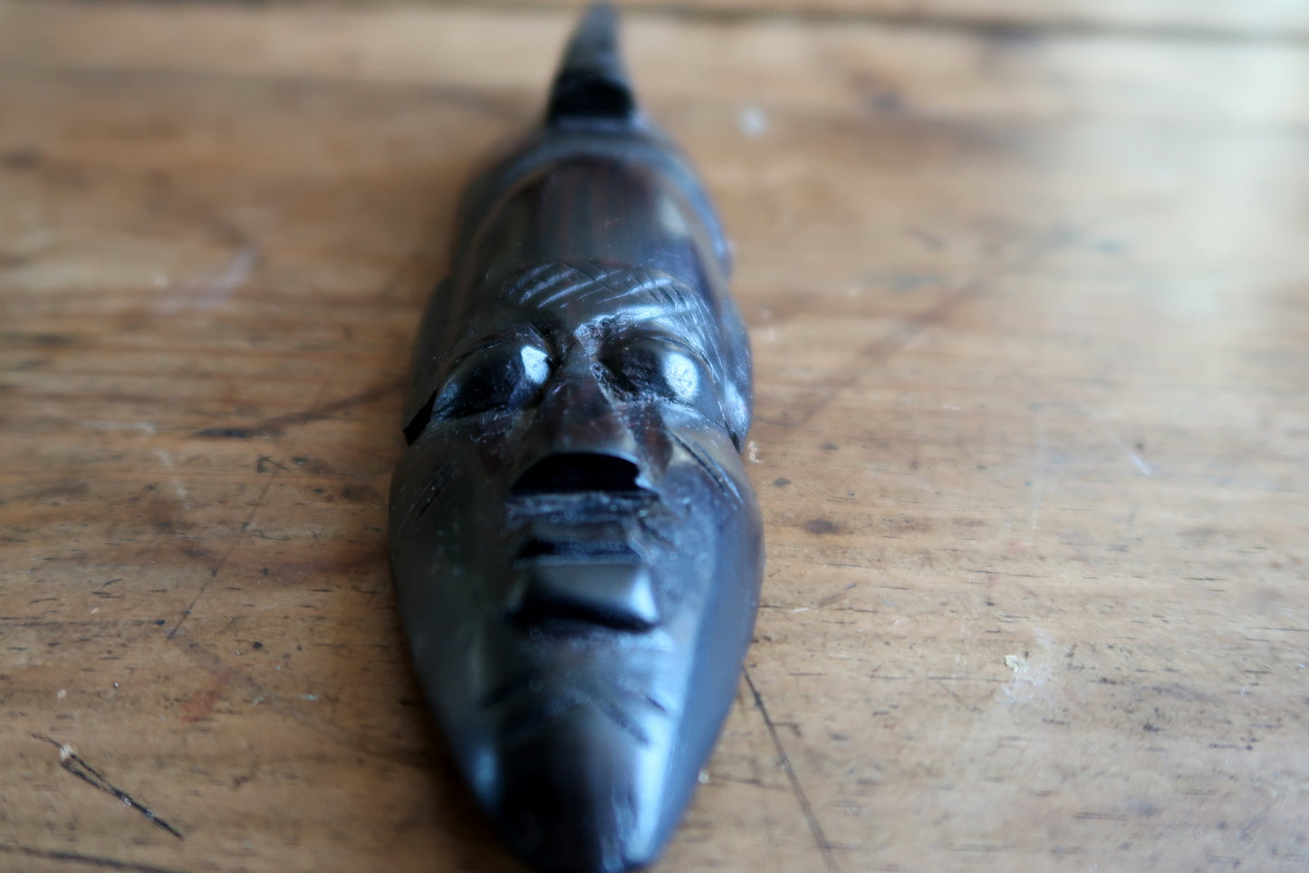 Detail of the geometric scarification marks on a carved African wood mask, showing crosshatch patterns on the forehead and chin and linear incisions along the jaw – traditional facial marking with social and spiritual significance.

