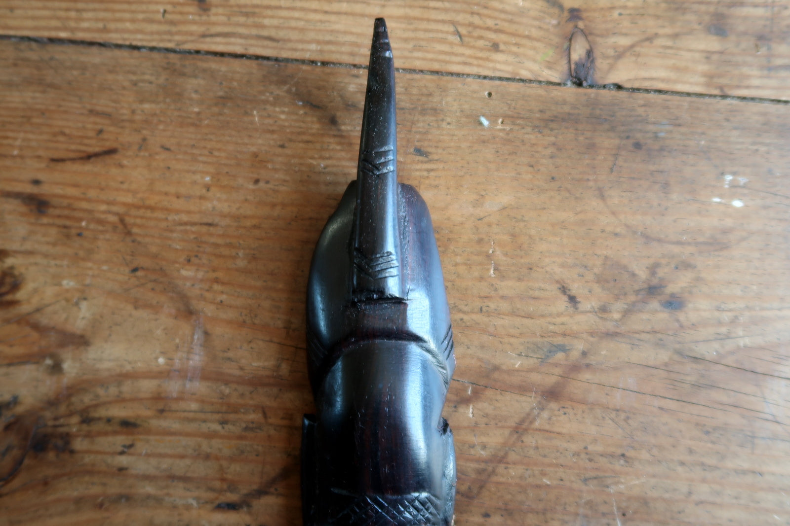 Full view of a miniature African carved mask displayed on a white background, showing the elongated face, tall horn/crest, polished ebonized front surface, and the characteristic serene, contained authority of Baoulé-influenced mask carving.

