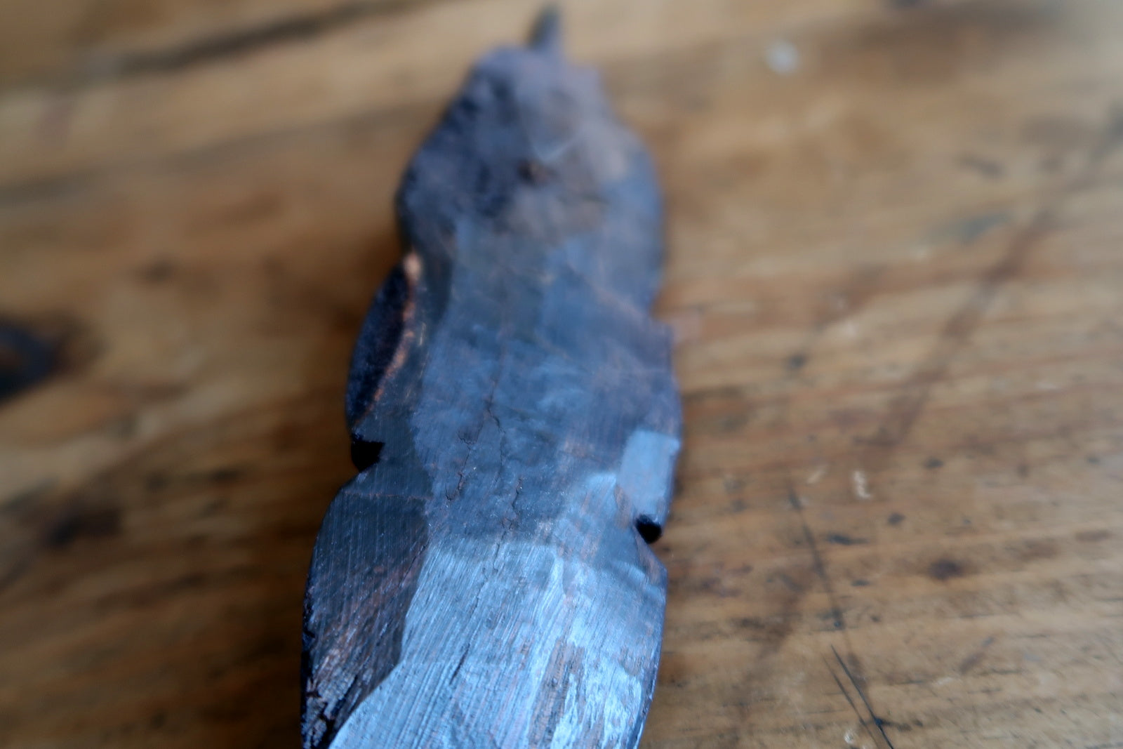 Side view of an ebonized wood face mask from West Africa, showing the elongated profile, tall crest, and the fine horizontal band separating the upper horn from the face, carved with parallel incisions.

