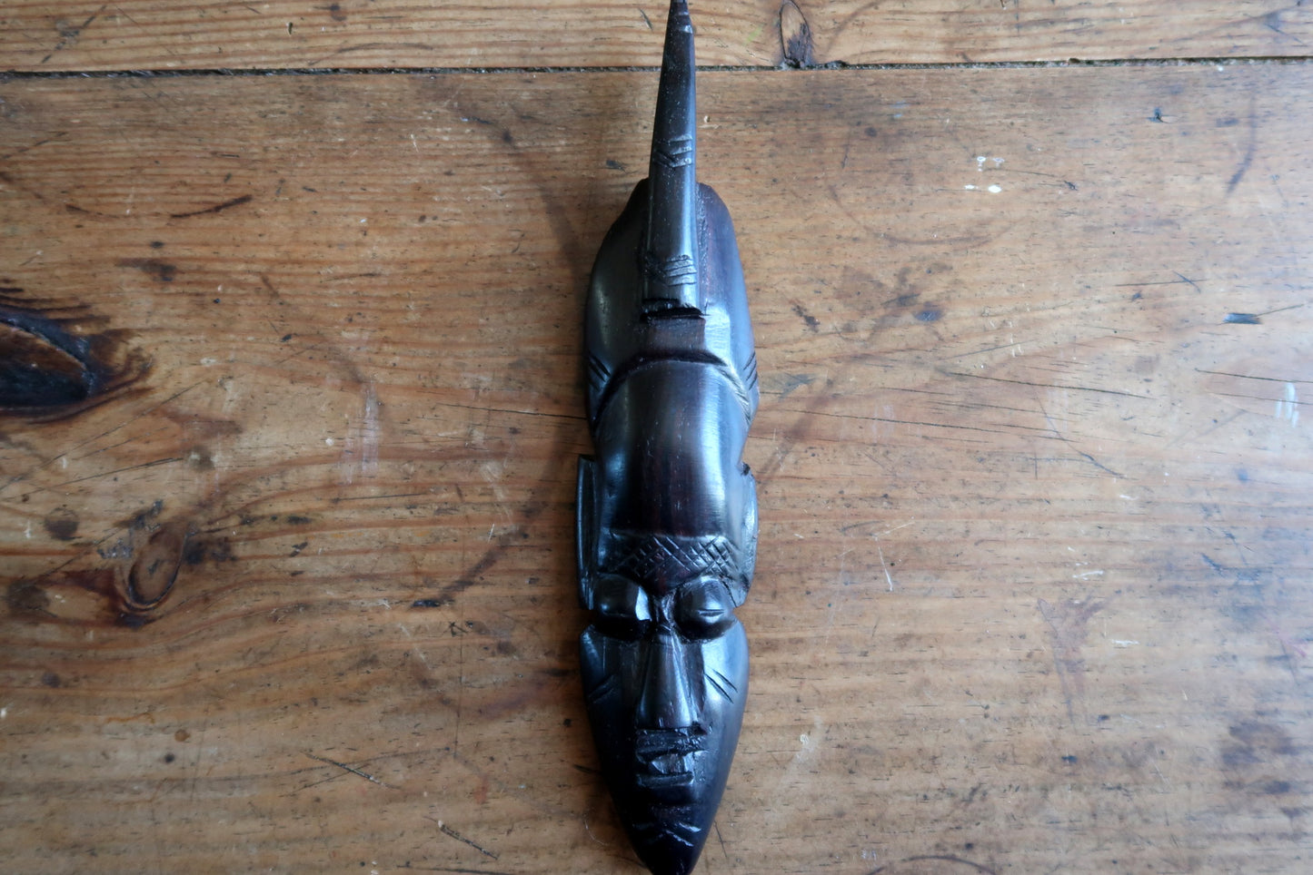 Rear view of a vintage African carved mask showing the unfinished reverse with grey coating flaking (invisible when displayed) and a wire hanging loop attached for wall display.

