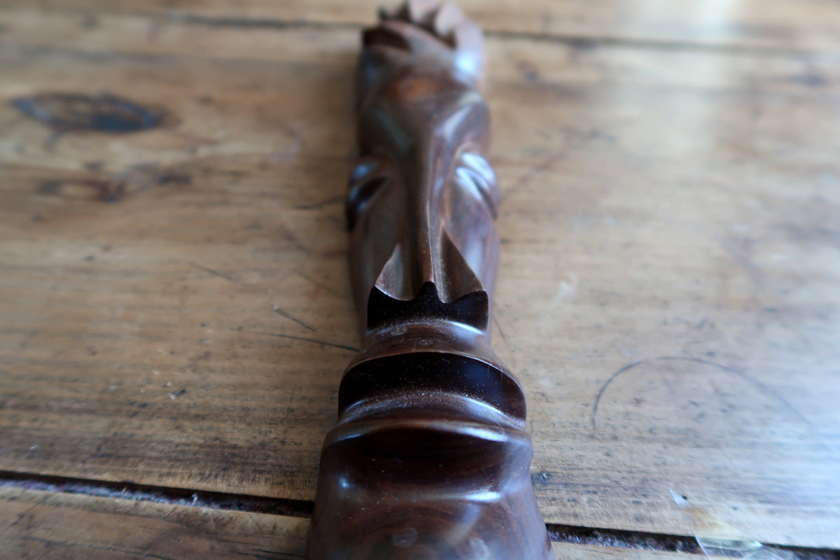African abstract carved mask displayed in natural side lighting, emphasizing the soft highlight reflections along its polished wooden surface.